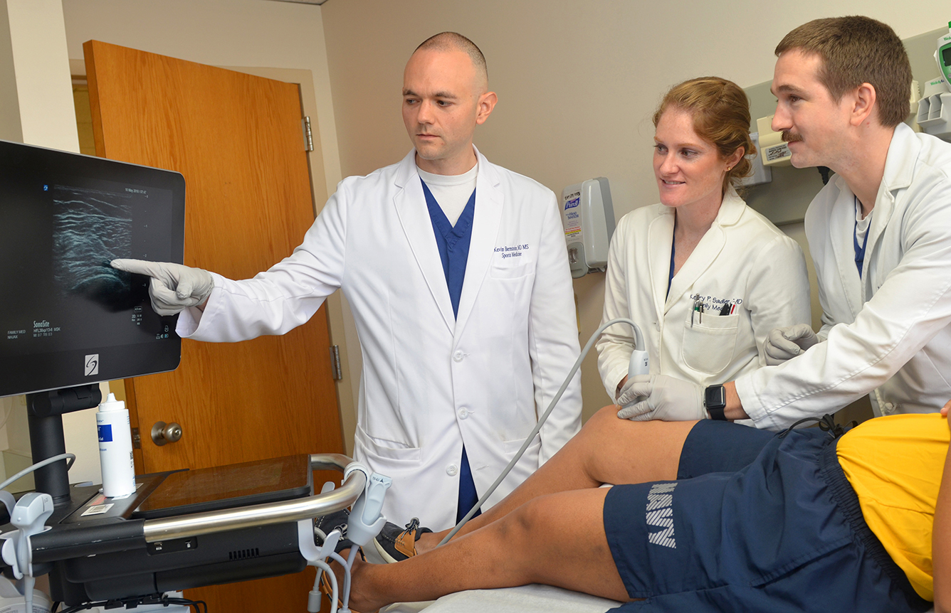 JACKSONVILLE, Fla. (May 10, 2018) (left to right) Sports Medicine Physician Lt. Cmdr. Kevin Bernstein, with Family Medicine Physicians Lt. Kerry Sadler and Lt. Paul Seales, examine a patient's knee at Naval Hospital Jacksonville's family medicine clinic. Patients can ask their primary care manager for a referral to Family Medicine Musculoskeletal Injections Clinic. The clinic provides sports medicine expertise and ultrasound-guided injections when appropriate for joint pain and function. (U.S. Navy photo by Jacob Sippel, Naval Hospital Jacksonville/Released).